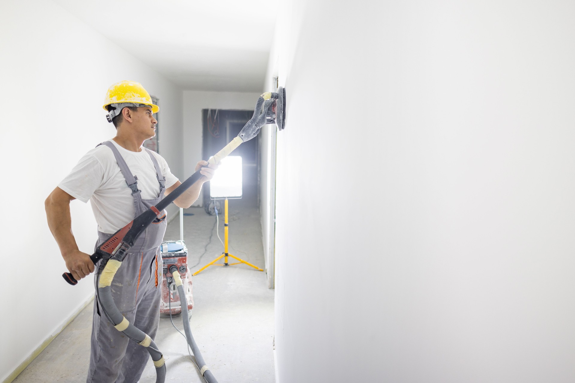 Caucasian male house painter using an sanding vacuum machine, while working on a construction site