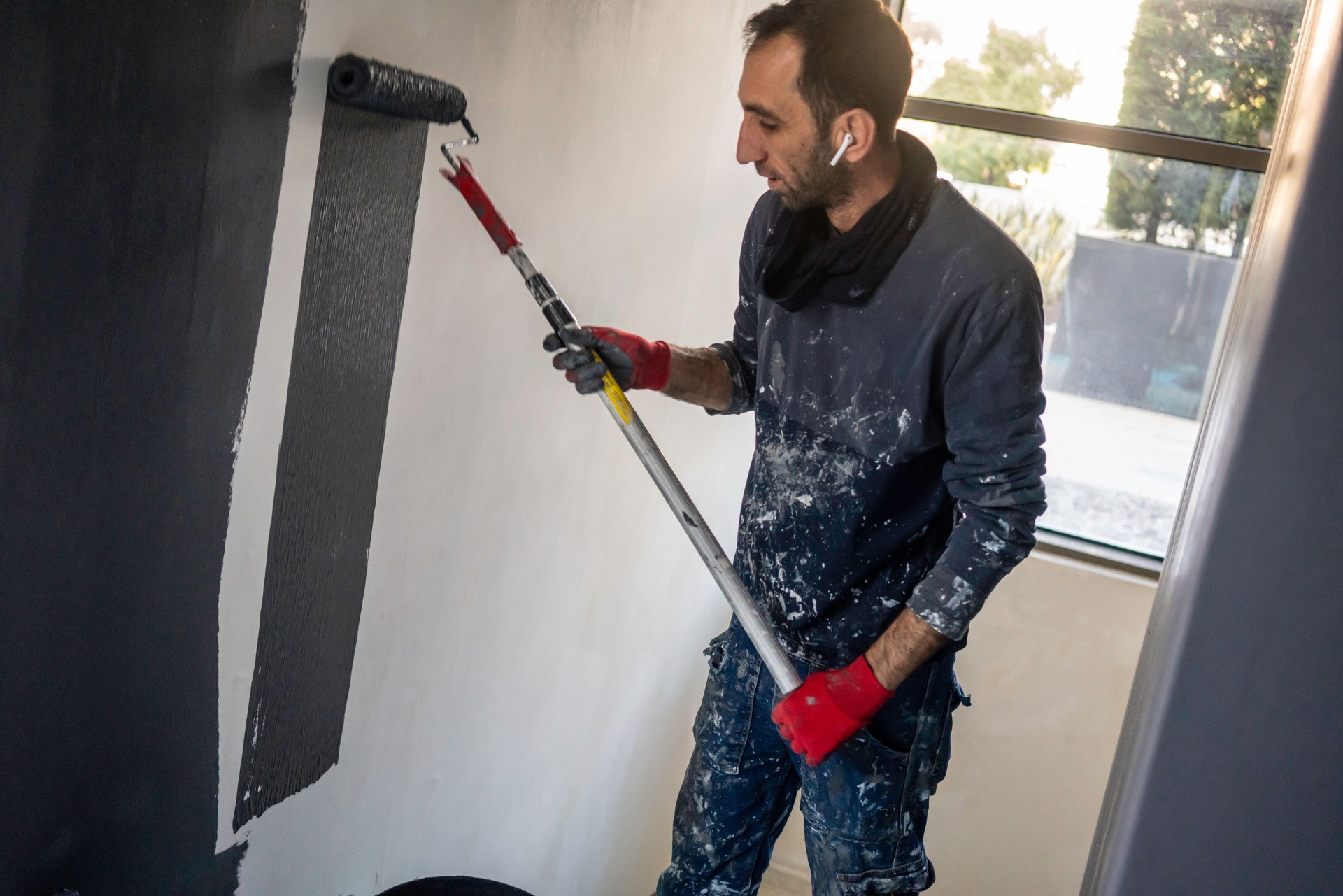 male blue collar worker is painting to wall with roller horizontal fixer upper home still